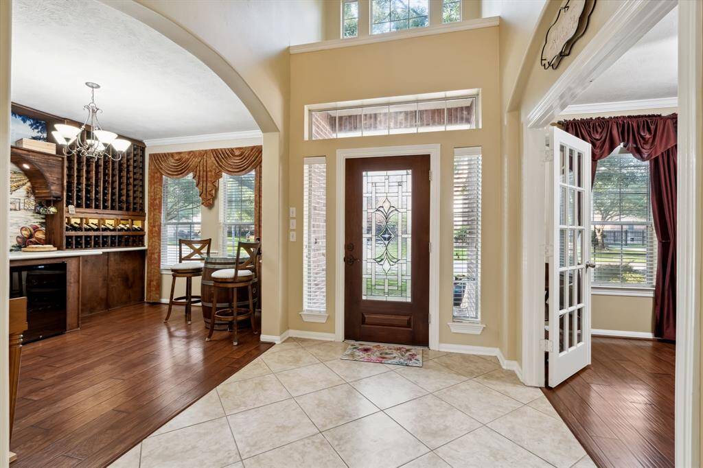 This inviting foyer features a decorative glass front door, high ceilings, and abundant natural light. It opens into a cozy wine room with elegant wood flooring and a wine storage nook.