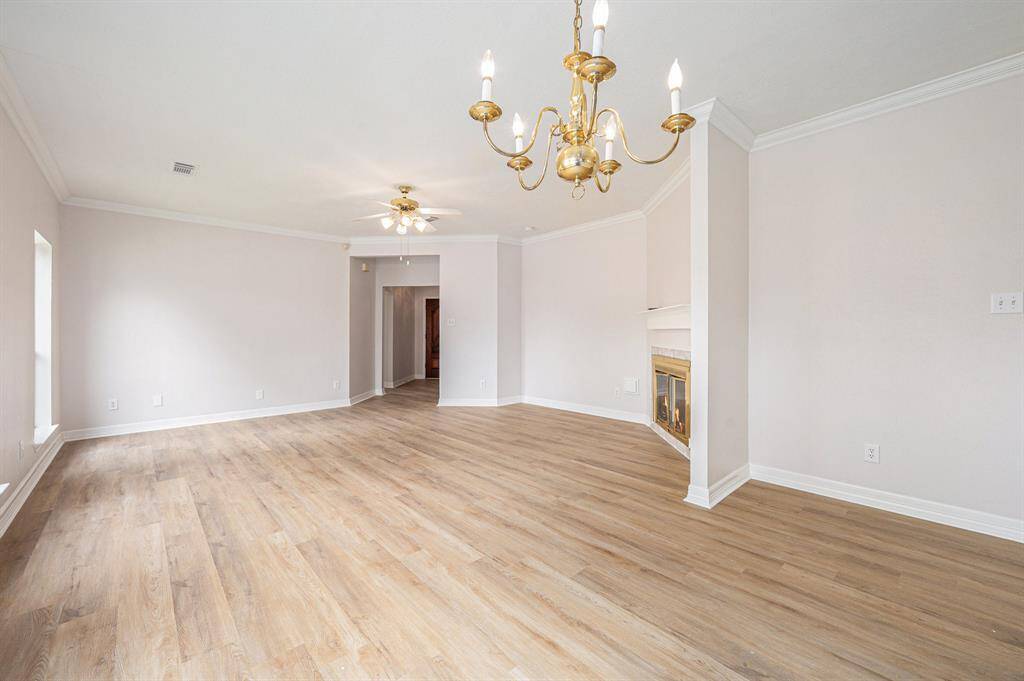 This spacious living area features light wood flooring, neutral walls, a classic chandelier, and a cozy fireplace, offering a bright and inviting atmosphere.