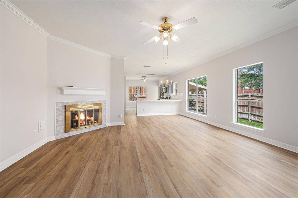 This spacious living area features elegant wood flooring, a cozy fireplace, and abundant natural light from large windows. The open layout flows seamlessly into a bright dining space and a modern kitchen, perfect for entertaining.