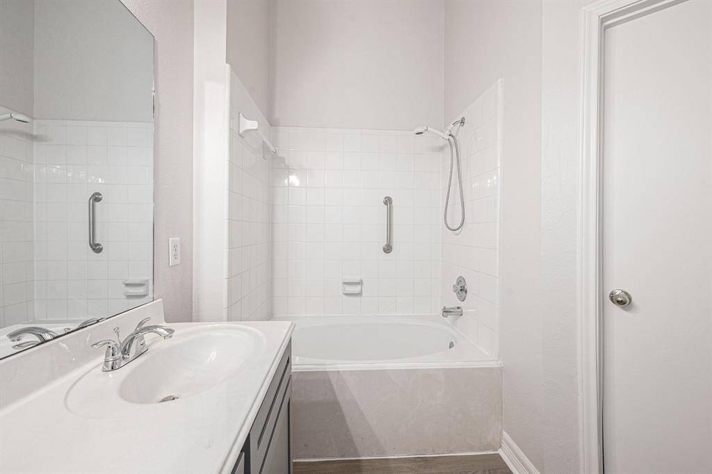 This primary bathroom features a clean, modern design with a white tiled shower-tub combo, a sleek vanity with a large mirror, and neutral walls for a bright, airy feel.