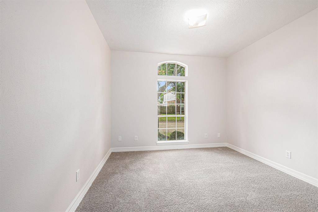 Bright, cozy room with neutral walls and carpet, featuring a large arched window that provides plenty of natural light and a view of the greenery outside. Perfect for a small office or bedroom.
