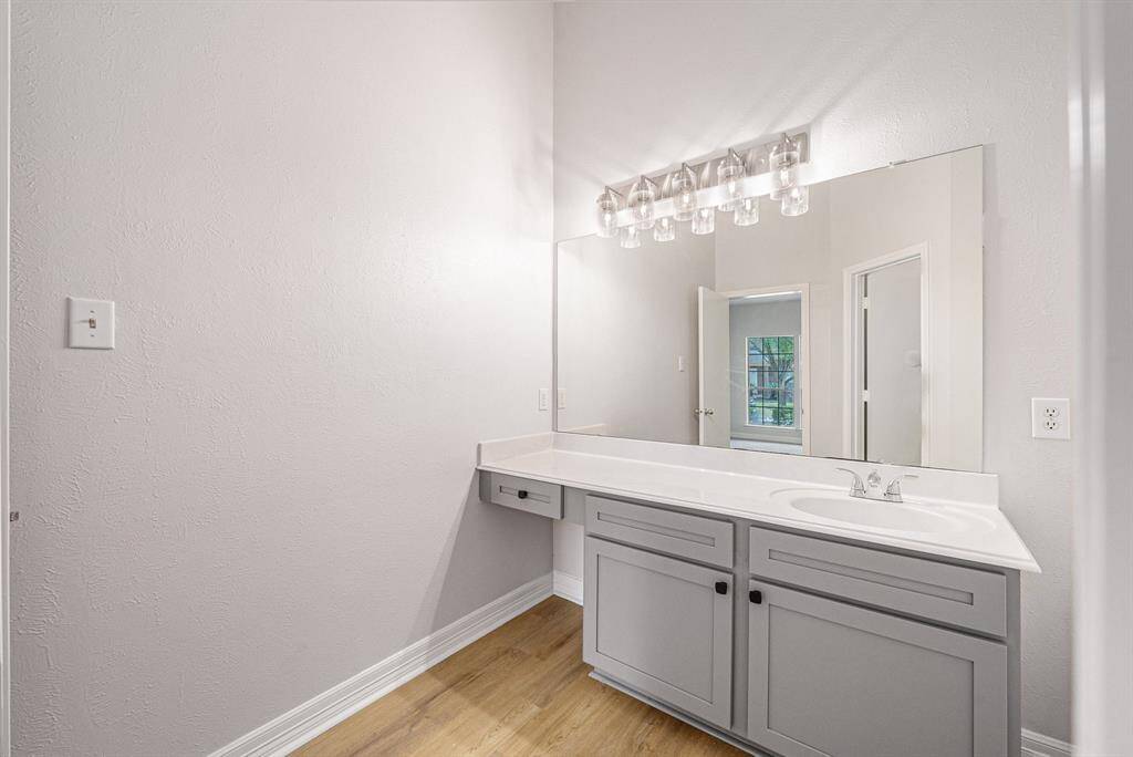 This bathroom features a modern design with a large mirror, stylish light fixture, and a sleek grey vanity with ample countertop space.
