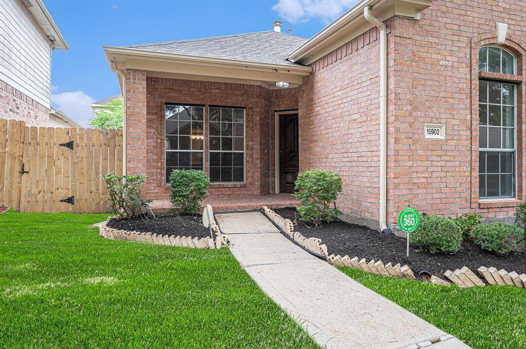 Charming brick home with a welcoming front entryway, featuring a well-maintained lawn, neatly trimmed shrubs, and a secure wooden fence.