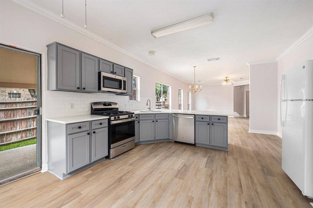 Bright, open-concept kitchen with modern gray cabinets, stainless steel appliances, and light wood flooring. Features a spacious layout with a central island, ample counter space, and direct access to the backyard through sliding doors. Perfect for entertaining.