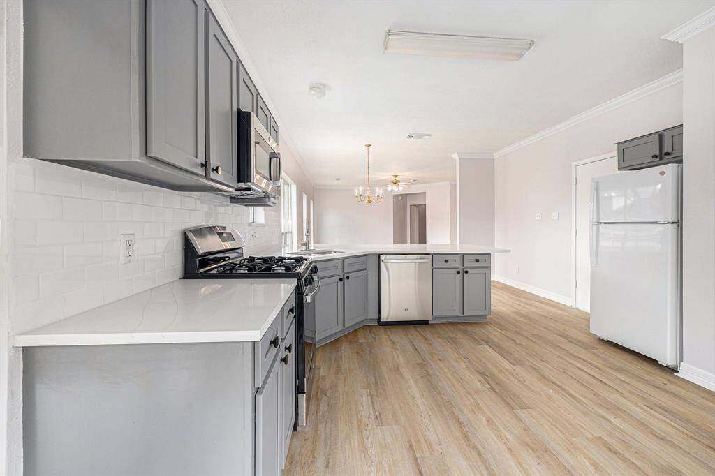 Spacious kitchen with modern gray cabinets, stainless steel appliances, and a central island. Features a bright, open layout with wood-like flooring and a neutral color palette, ideal for entertaining.