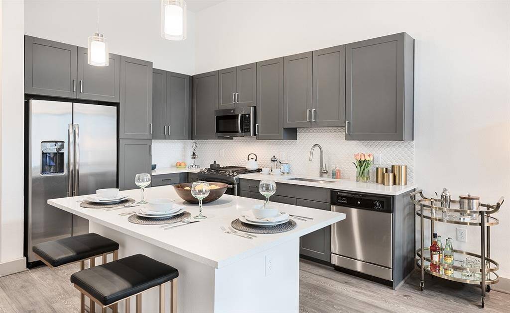 Sleek neutral flooring, cabinet tones with tile backsplash, stainless appliances.