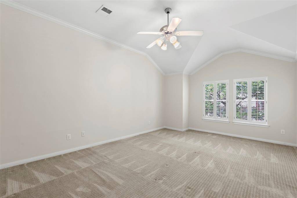 This spacious bedroom features neutral walls and carpet, a vaulted ceiling with a modern ceiling fan, and two large windows with plantation shutters, providing ample natural light