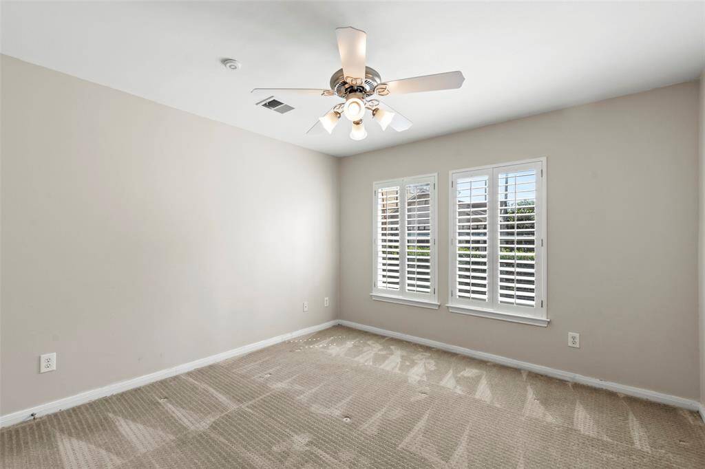Bright, airy bedroom with neutral walls and carpet, featuring a ceiling fan and large windows with plantation shutters