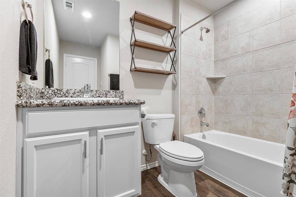 This clean, modern full guest bath features a tiled shower/tub combo, granite countertop, and sleek storage.