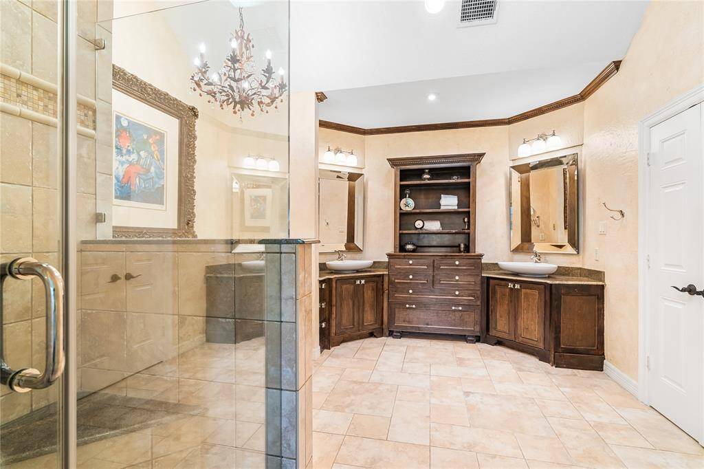 ELEGANT EN-SUITE BATHROOM WITH DUAL VANITIES, A CUSTOM WOOD CABINET TOWER, AND DESIGNER LIGHT FIXTURES.