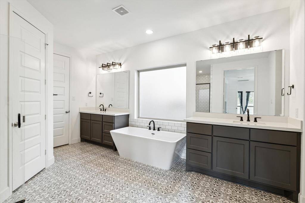 The primary bathroom features dual sinks, beautiful flooring, large frosted window, and a soaking tub.