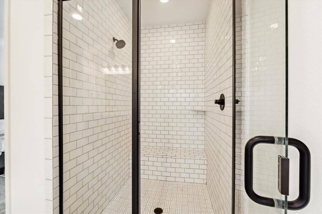 The primary bathroom also has a spacious walk-in shower with tile surround, sitting area, and glass door.