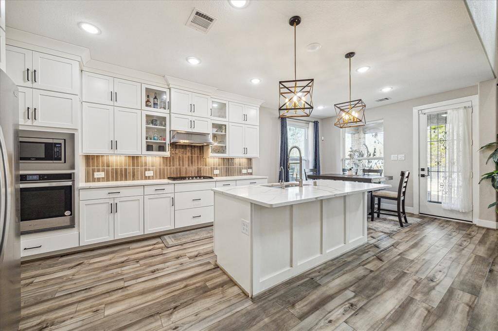 The kitchen features a large island with a sleek quartz countertop and a deep sink, illuminated by stylish geometric pendant lights. The floor-to-ceiling cabinetry provides ample storage, complemented by a modern backsplash and stainless steel appliances.