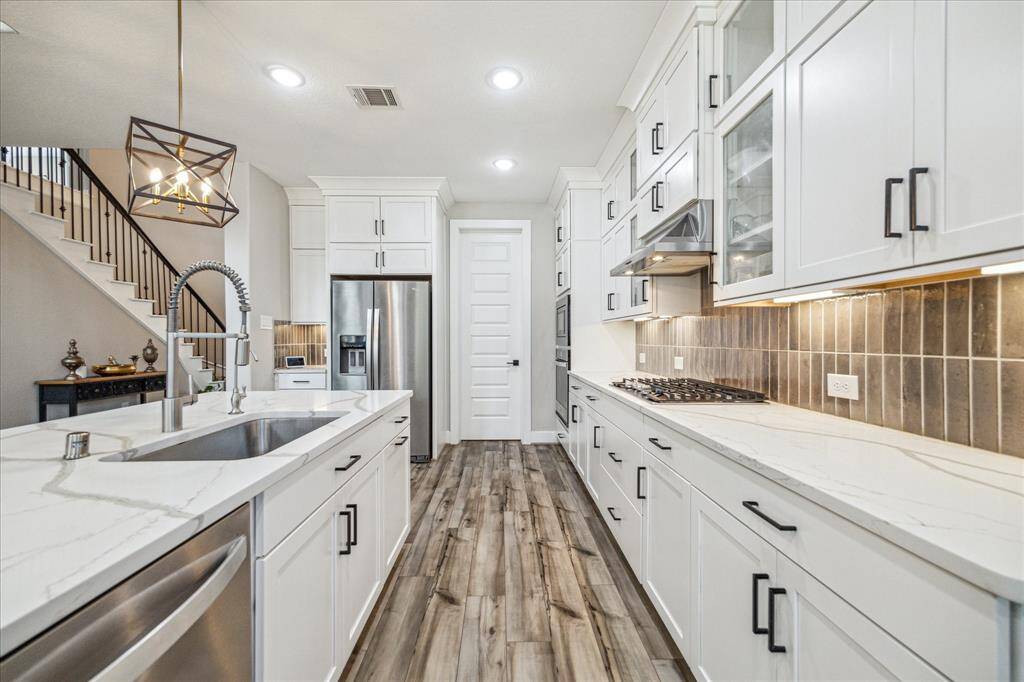 The kitchen features a galley-style layout with ample cabinetry and sleek quartz countertops that extend along both sides. A modern farmhouse sink with a high-arc pull-down faucet complements the stylish pendant lighting, enhancing the space's functionality and elegance.