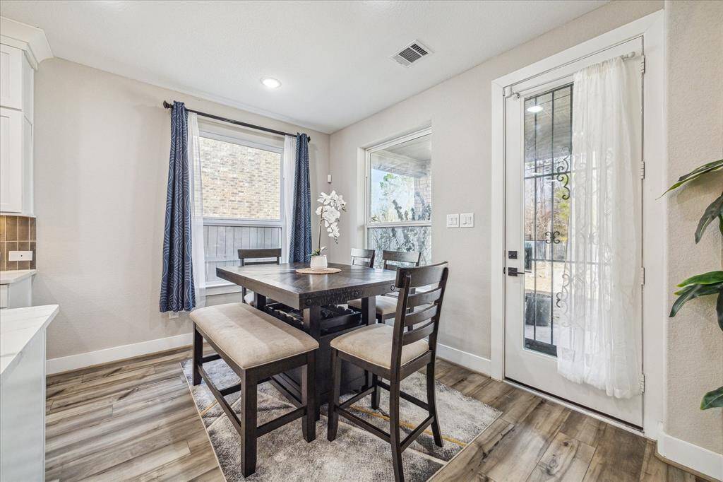 The dining area is filled with natural light from large windows and a glass-paneled door leading to the outdoor space. The neutral wall tones and elegant flooring create a warm and inviting atmosphere.