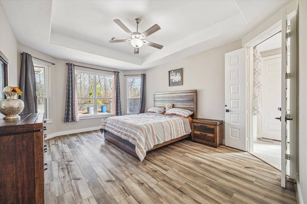 The primary bedroom features a spacious layout with large windows that allow for abundant natural light and scenic outdoor views. The tray ceiling with a modern ceiling fan enhances the room’s elegant design, creating a comfortable and airy retreat.