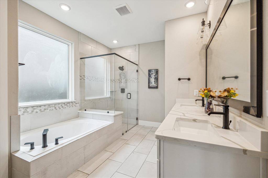 The primary bathroom showcases a luxurious design with a spacious glass-enclosed shower, a deep soaking tub, and elegant tile accents. A double vanity with sleek marble countertops and modern black fixtures enhances both functionality and style.