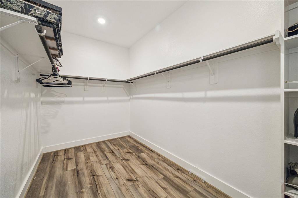 The primary walk-in closet offers ample storage space with dual hanging rods and built-in shelving for organization. Its bright white walls and recessed lighting create an open and inviting atmosphere.