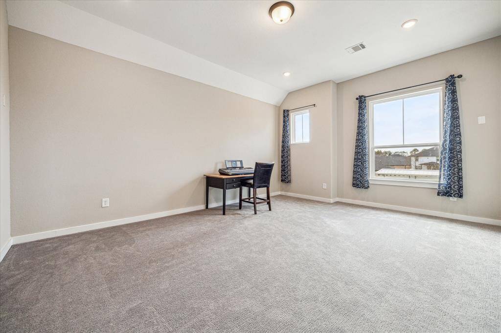 The media room features a spacious layout with soft carpeting and neutral-colored walls, creating a cozy atmosphere. Large windows allow for natural light while offering a pleasant view of the neighborhood.