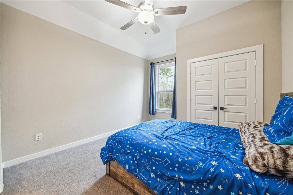 The upstairs bedroom features a neutral color palette with soft carpeting and a well-lit ambiance. A large window provides natural light and a view of the outdoors, while a double-door closet offers ample storage space.