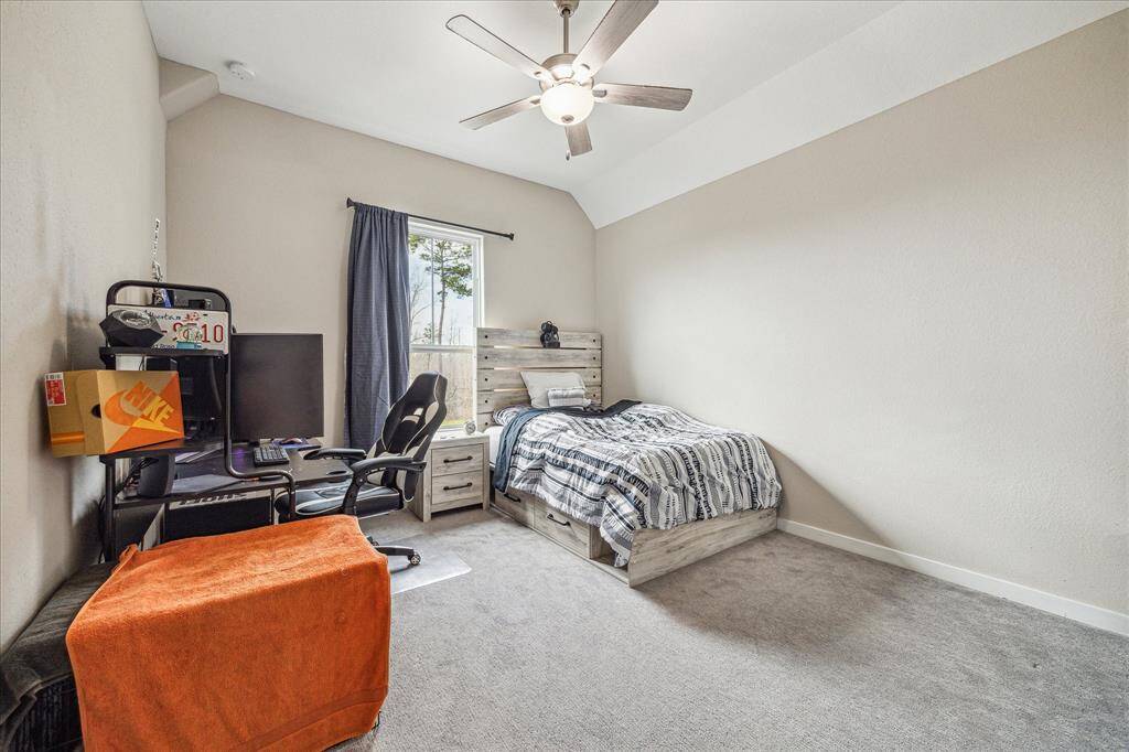 The second upstairs bedroom features a vaulted ceiling and a large window that allows natural light to brighten the space. Neutral-toned walls and soft carpeting create a cozy and inviting atmosphere.