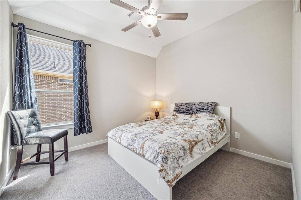 The third upstairs bedroom offers a cozy ambiance with soft carpeting and a neutral color palette. A large window with stylish curtains allows natural light to illuminate the space.
