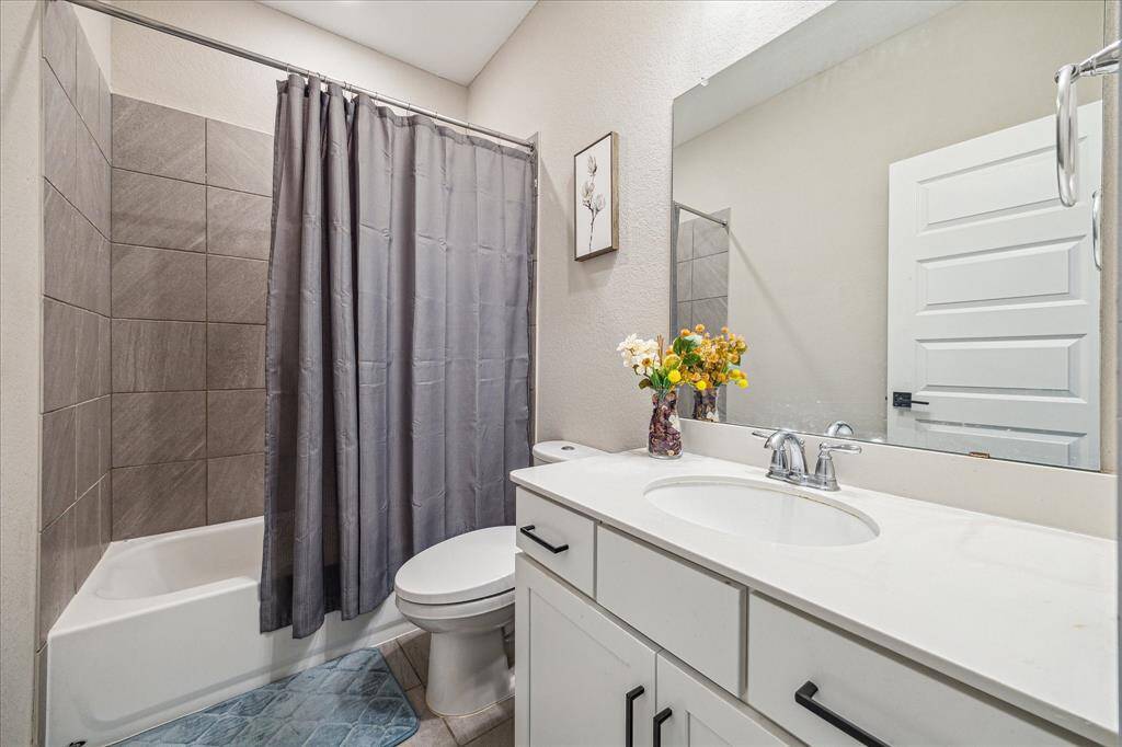 The upstairs bathroom features a sleek white vanity with ample storage and a polished quartz countertop. A large frameless mirror enhances the space, reflecting the soft neutral tones of the walls and modern fixtures.