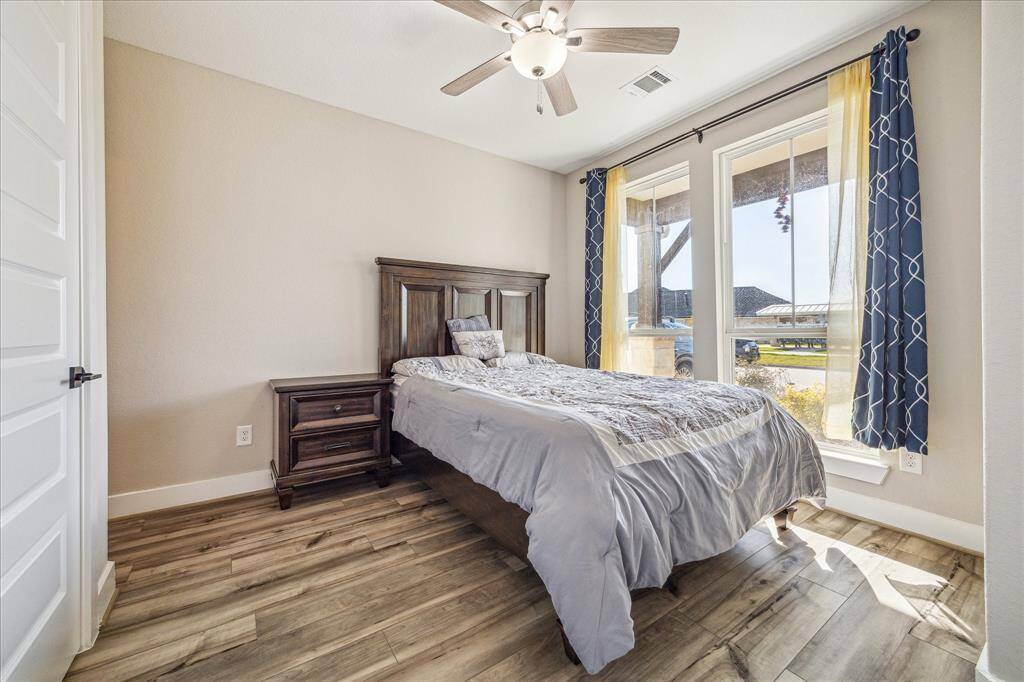 This is the second bedroom located on the first floor, featuring large windows that bring in plenty of natural light. The room has wood-look flooring and a neutral color palette, creating a warm and inviting atmosphere.