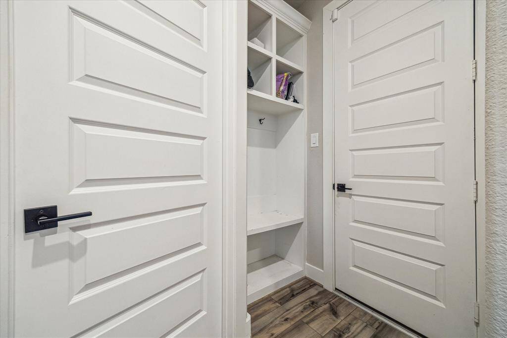 the mudroom on the first floor, featuring built-in white storage cubbies and hooks for organization. The space is framed by two paneled doors with modern black hardware, complementing the wood-look flooring.