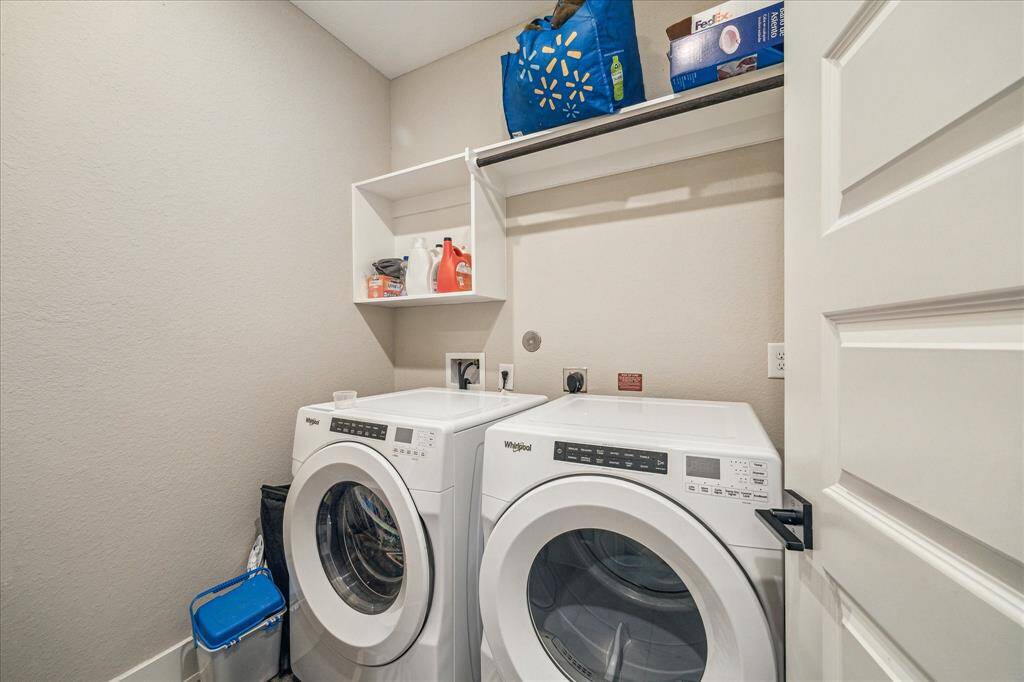 This is the utility room on the first floor, equipped with a front-loading Whirlpool washer and dryer. The space includes built-in shelving and a hanging rod for added storage and organization. (Washer and Dryer not included)