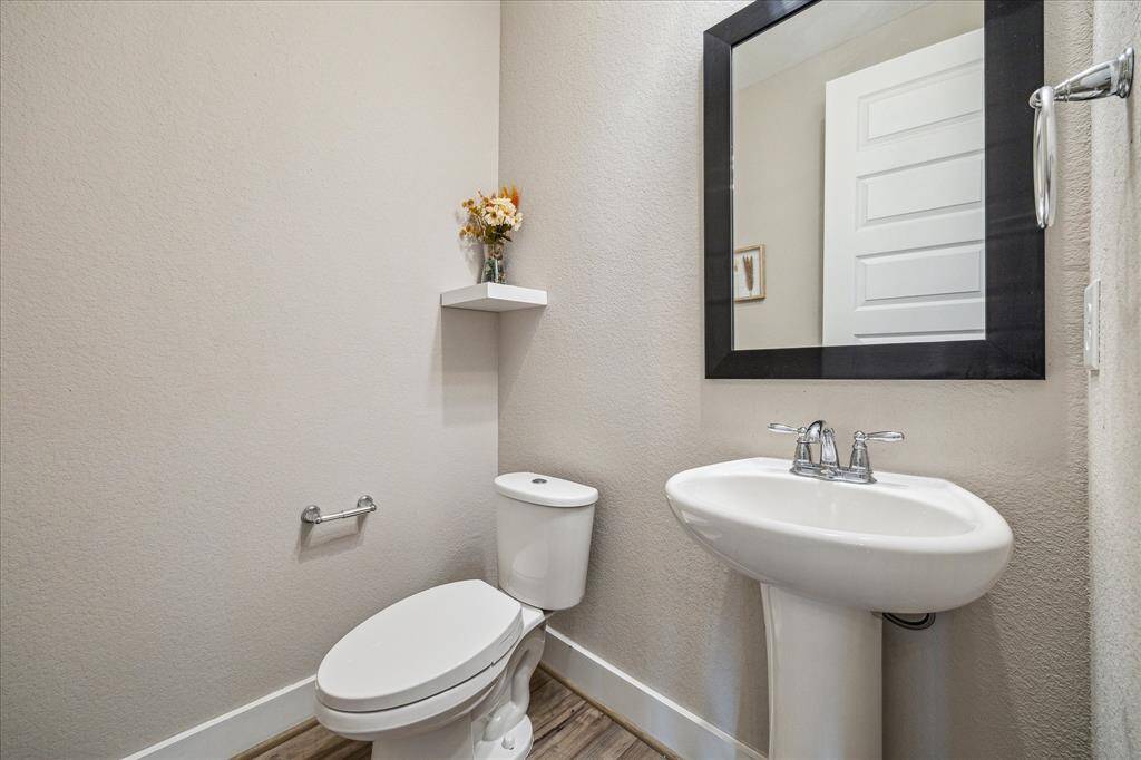 This is the half bath on the first floor, featuring a white pedestal sink with a chrome faucet. A black-framed mirror hangs above the sink, and a small floating shelf provides space for decorative accents.