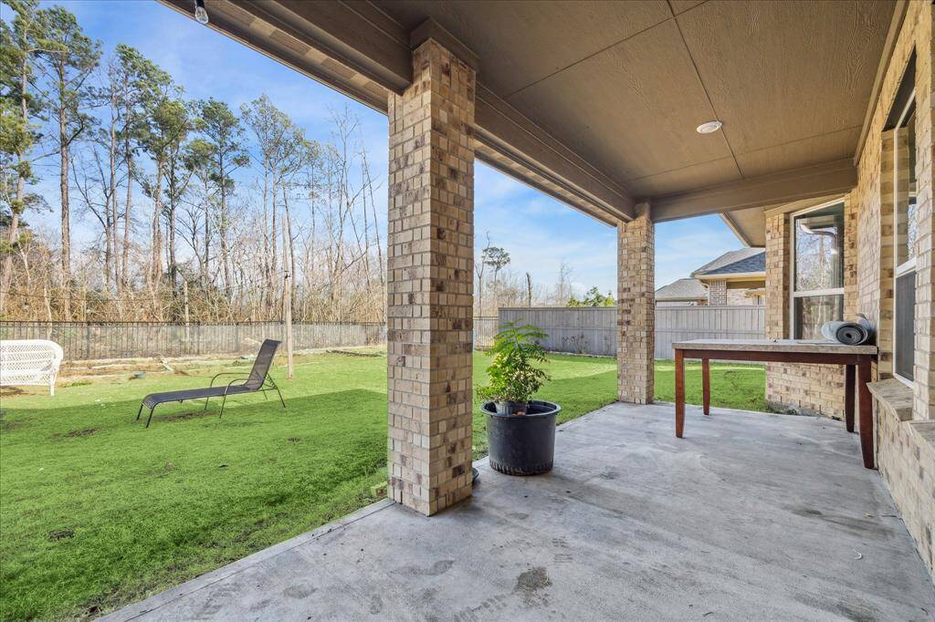 The back patio features a spacious covered area supported by brick columns, providing a shaded retreat. The backyard is enclosed by a combination of wooden and metal fencing, offering both privacy and a scenic view of the surrounding trees. Gas and water connection is available for outdoor kitchen.