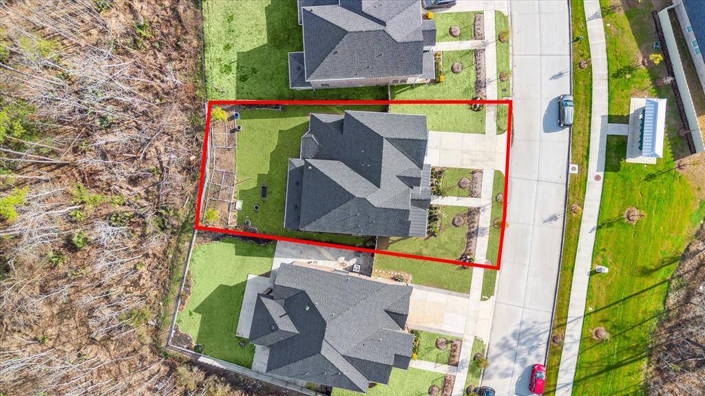 This aerial view highlights the home's well-defined lot, outlined in red, showcasing its spacious backyard and neatly landscaped front yard. The property is situated in a peaceful neighborhood with easy access to a sidewalk-lined street and nearby green spaces.