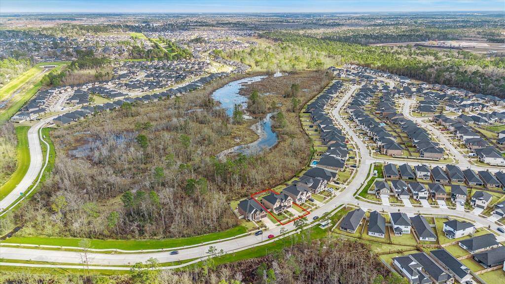 This aerial view showcases the home's striking facade with a blend of brick and stone accents, a welcoming front porch, and a well-manicured lawn. Nestled between two similar upscale homes, the property backs up to a serene wooded area, offering both privacy and scenic natural views.