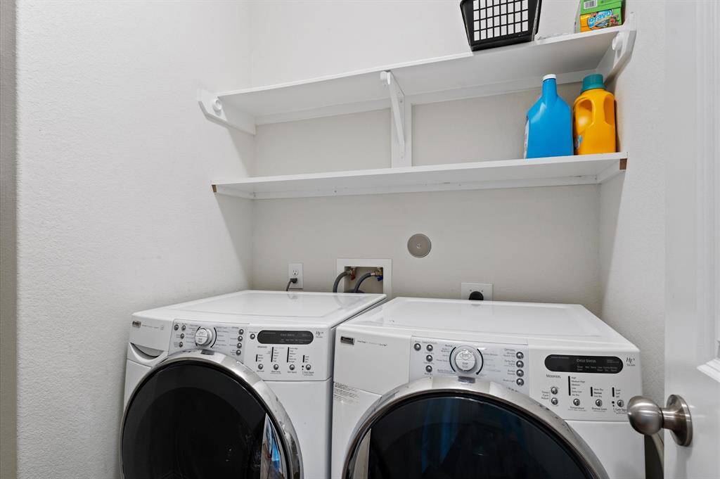 Laundry room with modern washer and dryer, white shelving above for storage, and a clean, bright aesthetic. Washer and dryer will stay with buyer.