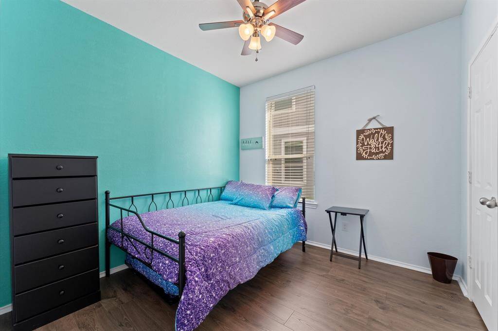 Photo of the second bedroom, featuring a vibrant teal accent wall and light blue walls, and a ceiling fan for comfort. The room has a window for natural light and wood-style flooring, offering a cozy and modern feel.