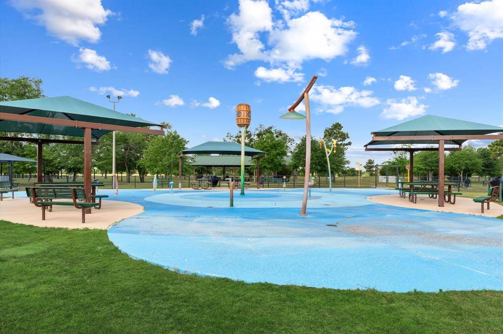 This photo features a community splash pad with shaded seating areas, picnic tables, perfect for family outings and outdoor activities.