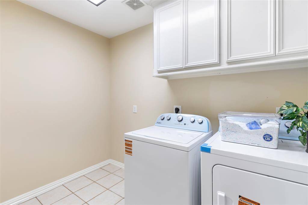 This spacious inside laundry room is both practical and organized, featuring ample cabinet space for storage and plenty of room for a secondary fridge.