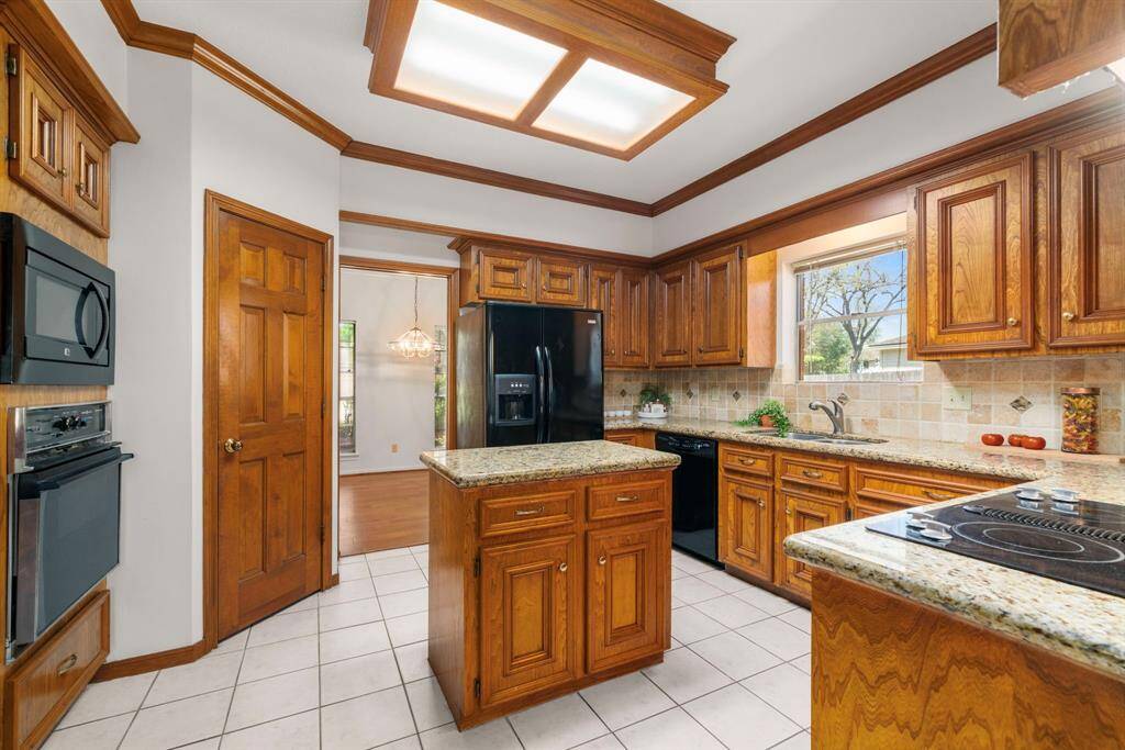 This view of the kitchen features the tiled floors and ample natural light from a large window, creating a cozy and functional cooking space.  Also, notice the counter-depth refrigerator/freezer that will stay with the home!