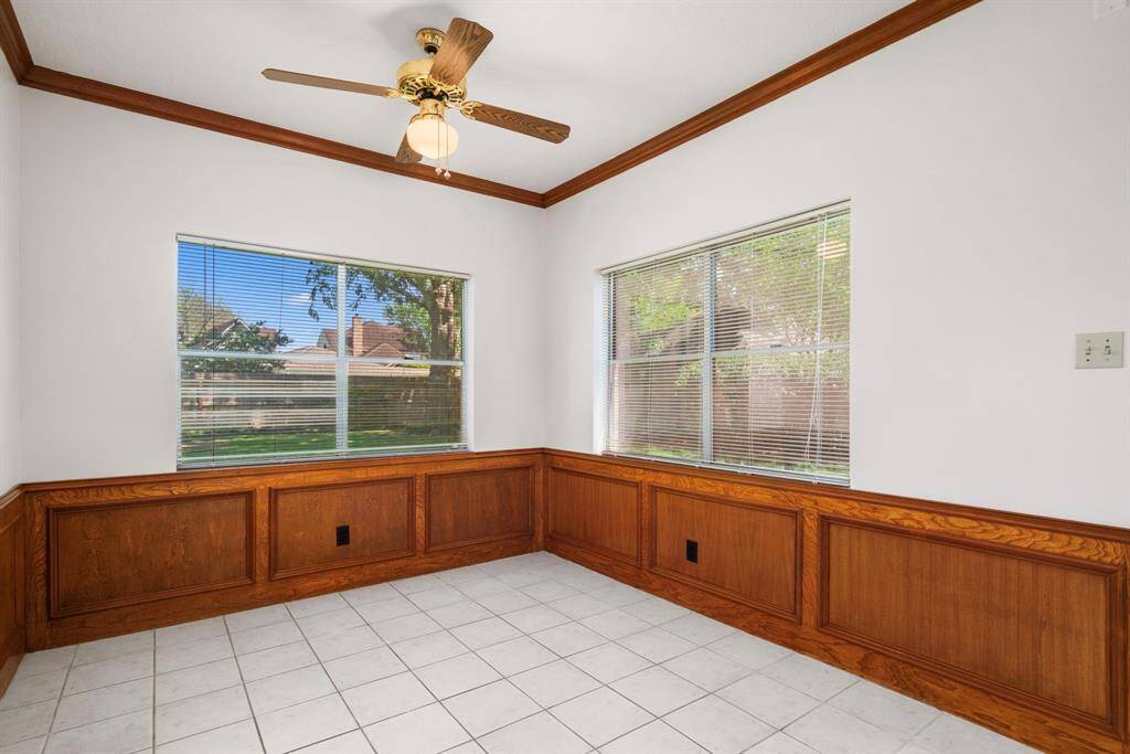 The sunny breakfast room features large windows with blinds, white walls, & elegant wood paneling. It has a ceiling fan & light, with tiled flooring, offering a bright and inviting space with a view of the fabulous backyard!