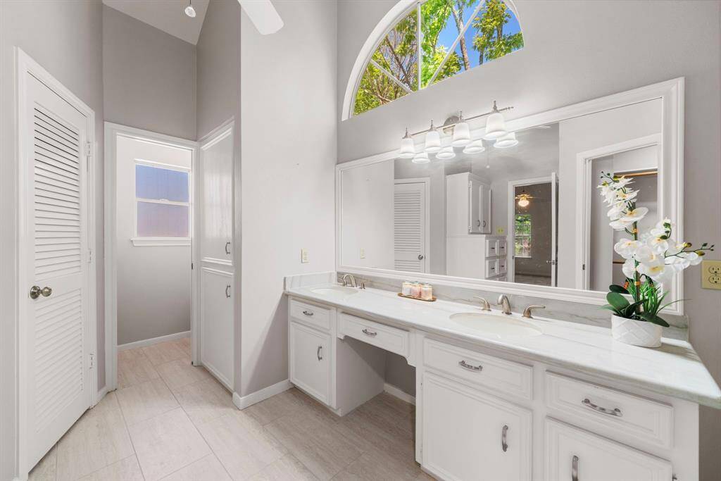 the  Primary Bathroom features a spacious double vanity with elegant fixtures, a large mirror, and ample cabinet storage. Natural light streams through a high arched window, creating a bright and welcoming atmosphere.