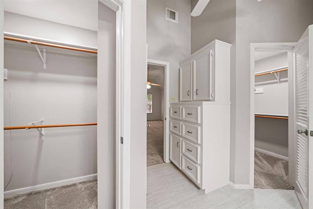 This view of the entry to the Primary Bathroom showcases the two spacious walk-in closets with ample shelving and hanging space. It also features built-in drawers and cabinets for linens and additional storage, and the neutral color scheme enhances the room's brightness.