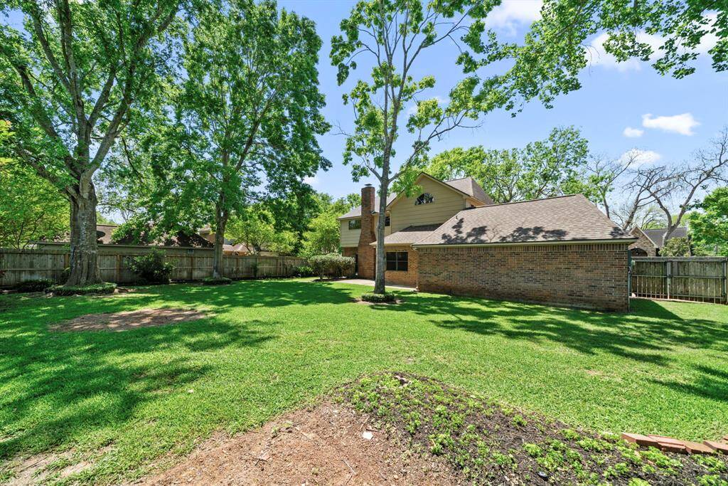 Spacious backyard with lush green lawn and mature trees, offering ample shade and privacy. Notice the extra space on the garage side of the house.  This would be perfect for a dog run or garden!