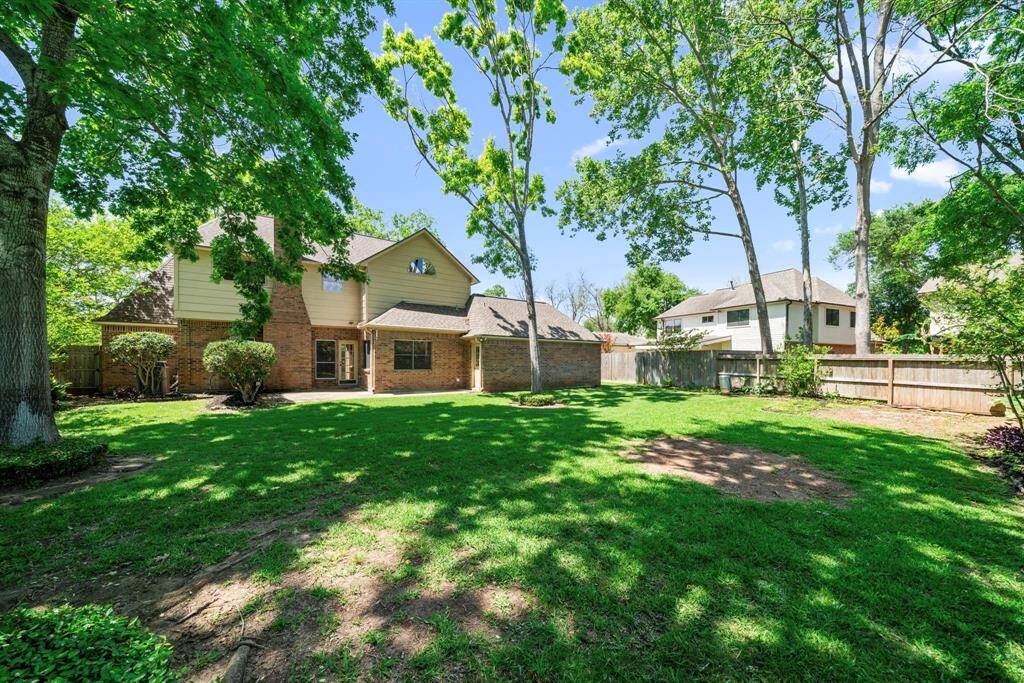 Spacious backyard with lush green lawn and mature trees, providing shade and privacy.  Fenced perimeter ensures security and a tranquil atmosphere.