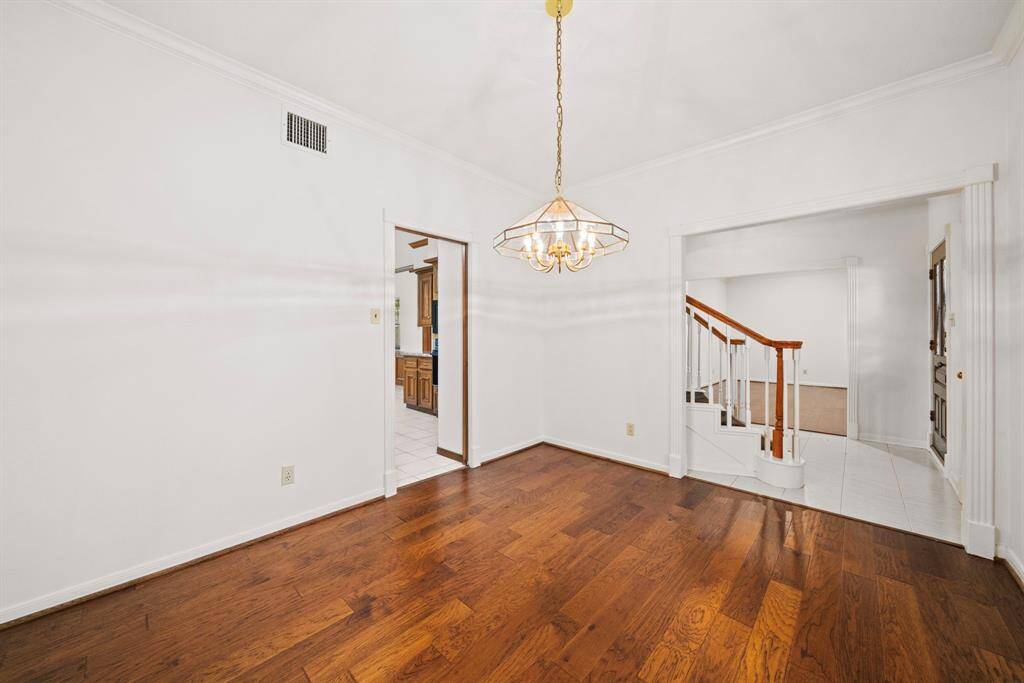 Another view of the bright dining area with hardwood floors, shows access to the kitchen and living room. Stairs with a wooden handrail lead to the upper level.