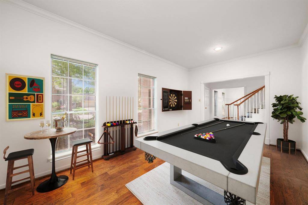 This photo showcases the bright & inviting formal living room.  The photo has been virtually staged to be a recreation room featuring a sleek pool table, dartboard, and a cozy bar table with stools. Large windows provide ample natural light, highlighting the room's hardwood flooring. It is a perfect space for entertaining!