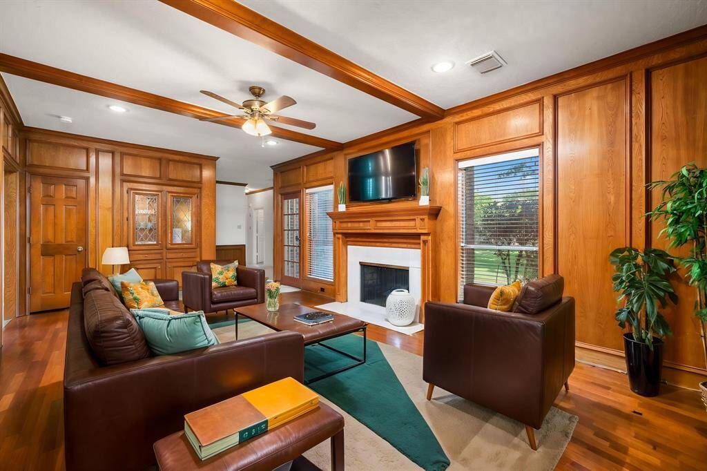 This inviting family room features rich wood paneling, a cozy fireplace with gas logs, a built-in wet bar, and ample natural light from large windows. The space is virtually staged with vibrant decor, creating a warm and welcoming atmosphere.