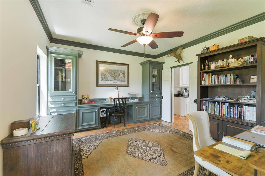 Office/workspace with custom built-in desk and cabinets, ceiling fan, accent crown molding and double door entry.