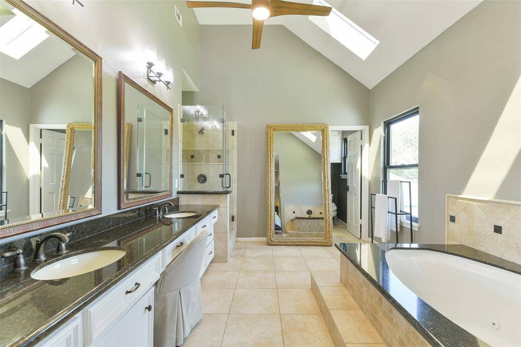 Primary bathroom with dual sinks, jetted stand-alone tub, step in shower, and newly installed 2024 skylights.  Note the beautiful ceiling fan.