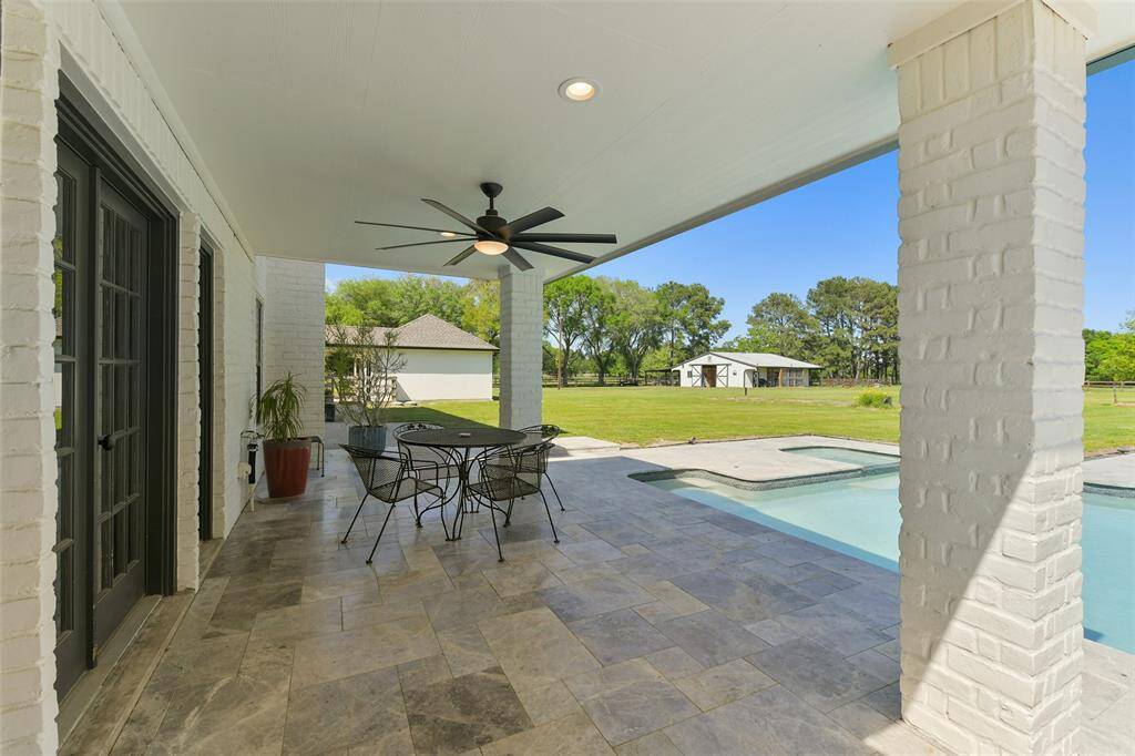 Extensive covered back patio with door access from kitchen and living room has marble flooring and extra large outdoor ceiling fan.